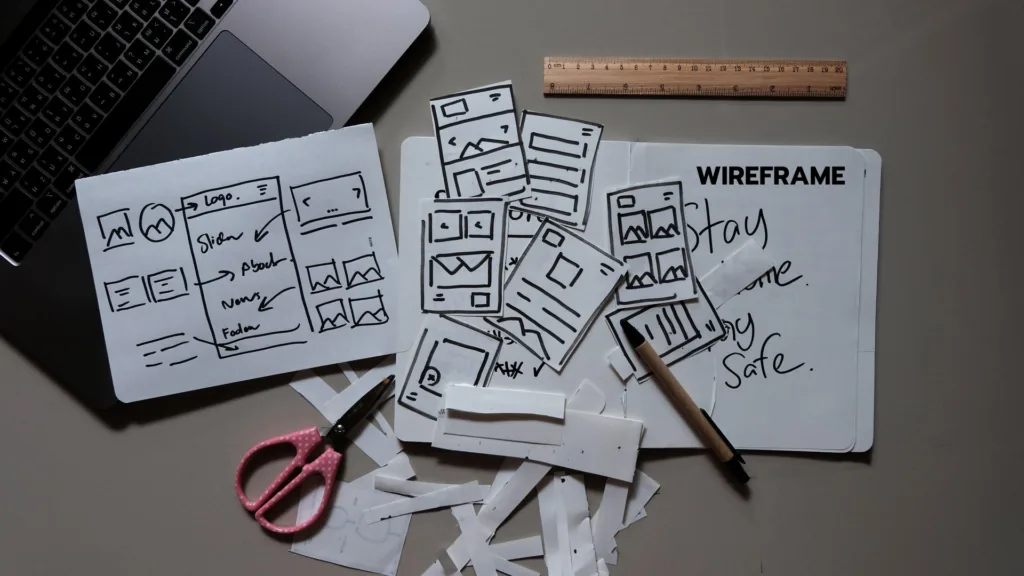 Contratar un diseñador web: bocetos de la estructura de una página web sobre la mesa junto a un portátil
