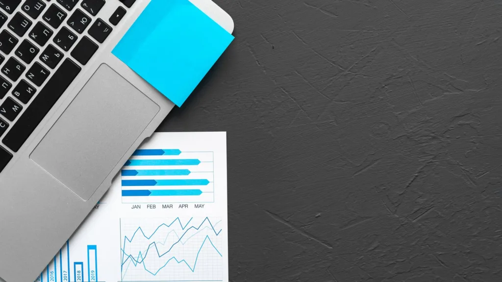Portátil y gráficos impresos sobre mesa oscura: cuadro de mando con KPIs de marketing digital de una pyme